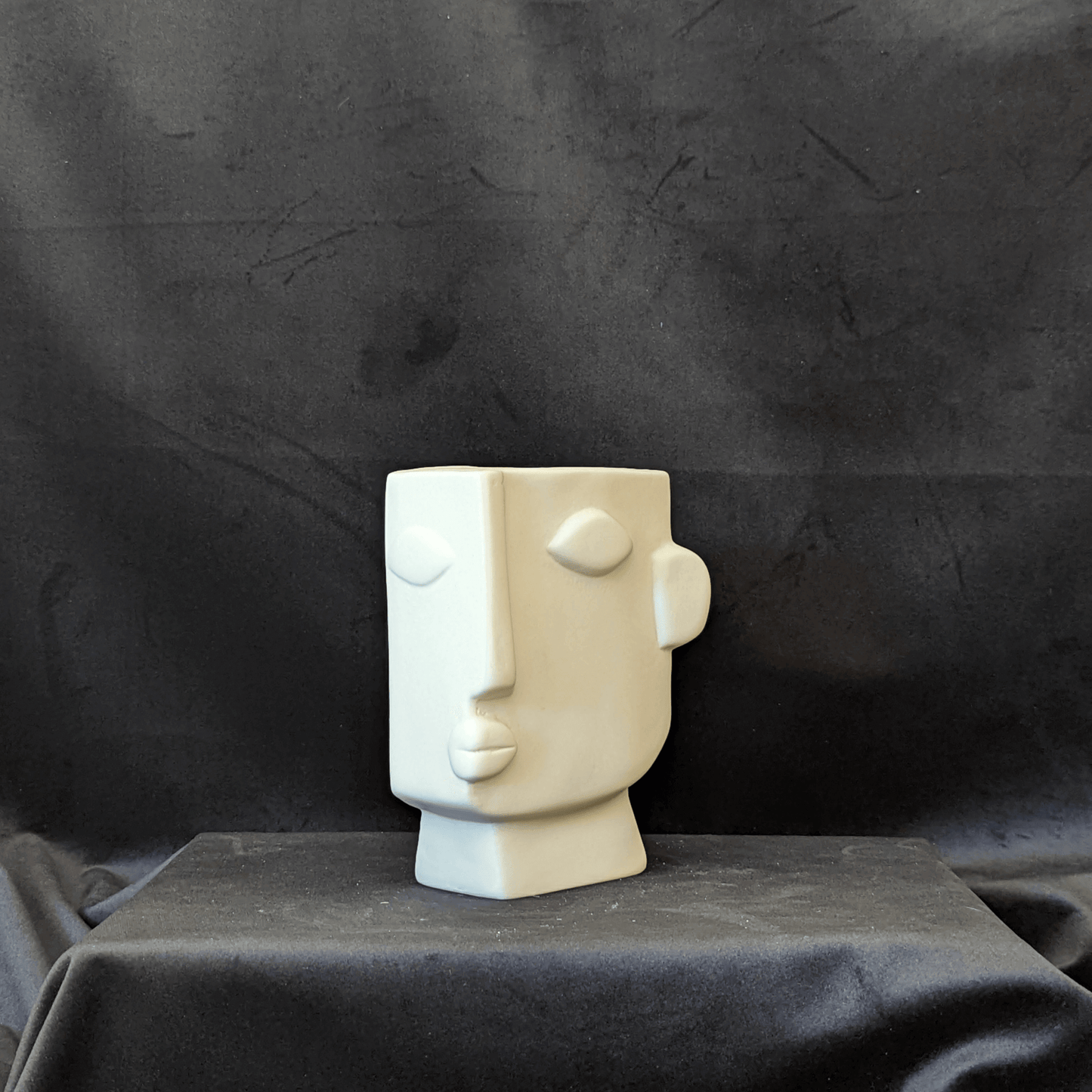 Cream vase with an artistic expression of a human face. It is square in shape with the face on a 3/4 angle.