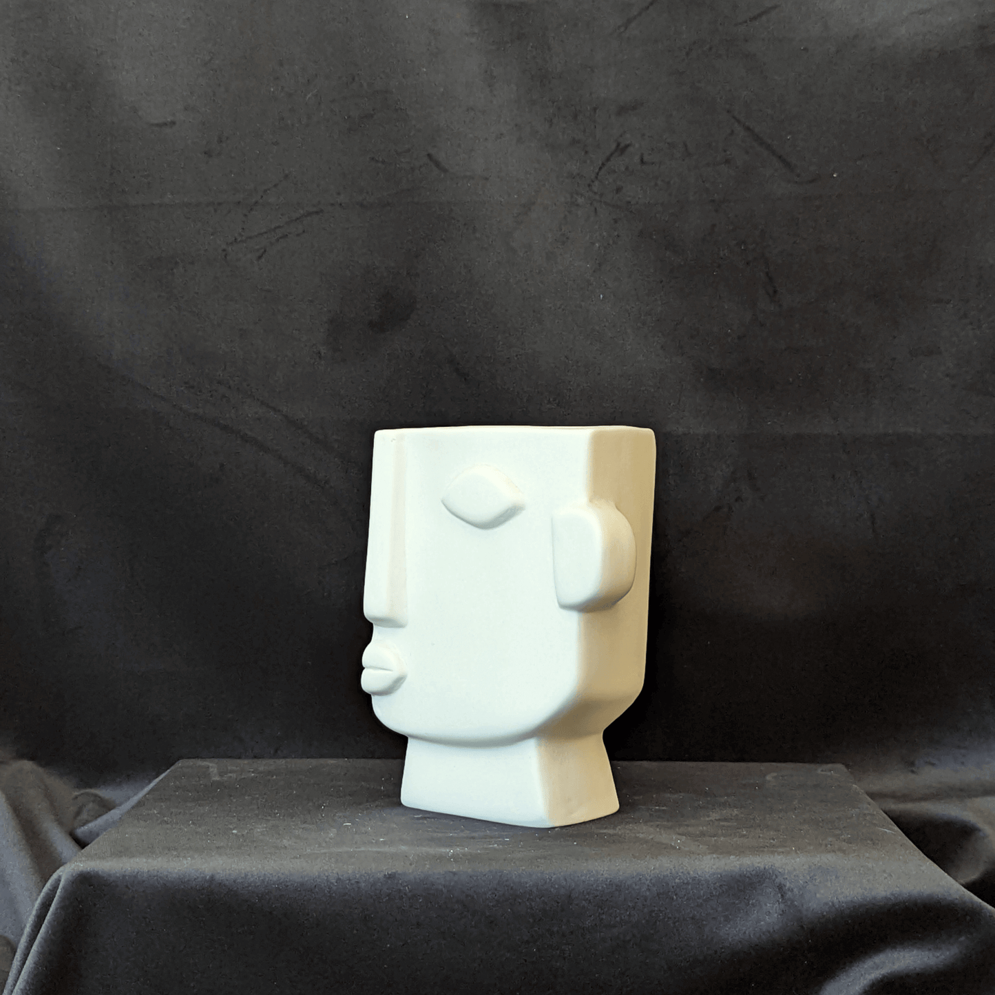 Cream vase with an artistic expression of a human face. It is square in shape with the face on a 3/4 angle.